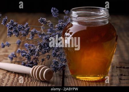 Miel dans un pot en verre, une cuillère pour le miel, fleurs de lavande sur une vieille table en bois. Arrière-plan sombre. Banque D'Images