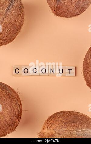 Brunir les fruits de la noix de coco tropicale entière sur fond de couleur. Noix de coco et inscription noix de coco en cubes de bois. Flat lay et vue de dessus. Banque D'Images