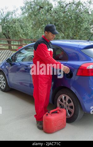 Image d'un mécanicien en combinaison comme il verse un additif dans le réservoir d'une voiture. Référence au carburant coûteux Banque D'Images