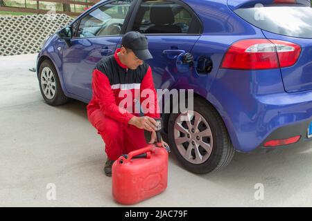 Image d'un mécanicien en combinaison comme il verse un additif dans le réservoir d'une voiture. Référence au carburant coûteux Banque D'Images