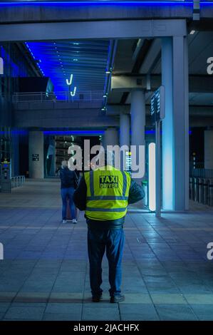 Portrait arrière d'un chauffeur de taxi debout dans le terminal 2 de l'aéroport de Manchester, en attente des clients. Banque D'Images