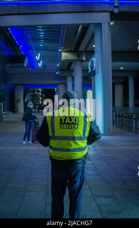 Portrait arrière d'un chauffeur de taxi debout dans le terminal 2 de l'aéroport de Manchester, en attente des clients. Banque D'Images