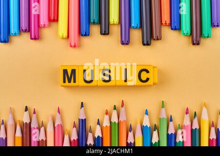 Le mot MUSIC écrit sur des cubes jaunes sur fond de couleur. Composition de pose plate avec marqueurs colorés. Banque D'Images
