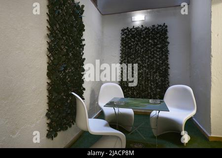 Petite terrasse intérieure avec un sol en herbe synthétique, des treillis de canne et des plantes et une table en métal avec chaises en résine blanche Banque D'Images