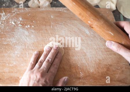 Une femme roule de la pâte avec une broche sur une planche à découper en bois. Boulettes faites maison. Banque D'Images