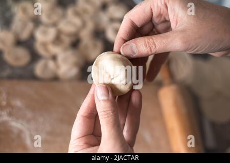 Une femme sculpte des boulettes de pâte avec garniture de viande dans la cuisine. Cuisson de délicieux boulettes maison. Banque D'Images