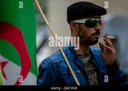 Montréal, Canada. 28th mai 2022. Un manifestant algérien tient le drapeau algérien alors qu'il fume une cigarette pendant la manifestation. Quatre ans après son entrée dans la diaspora algérienne, le mouvement Hirak continue de lutter pour la démocratie à Montréal. Organisé par tous nos Unis pour notre Algerie, des centaines de manifestants se sont rassemblés devant le Consulat algérien pour demander la destitution des dirigeants politiques actuels, dirigés par le président Abdelmadjid Tebboune. Invoquant la corruption chronique et l'absence de résolutions prévoyables, les manifestants ont qualifié le gouvernement de gouvernement mafieux. Crédit : SOPA Images Limited/Alamy Live News Banque D'Images
