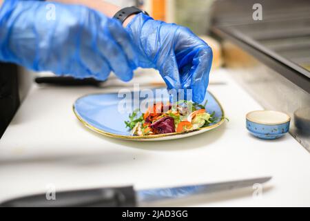 Gros plan d'une personne portant des gants de protection jetables mettant de la salade sur une assiette dans un café Banque D'Images