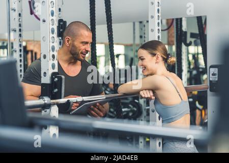 Une femme de fitness écrit un plan d'entraînement avec un entraîneur et riant à la salle de gym. Photo de haute qualité Banque D'Images