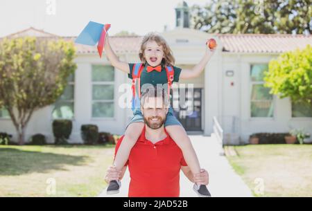 L'homme et l'enfant excités surpris de son porcgyback près de l'école. Le père et le fils courent avec le père après être revenus de l'école. École, famille, éducation et Banque D'Images