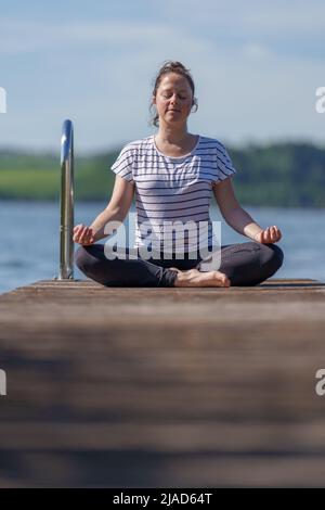 Femme assise à pieds croisés sur un quai méditant, Wallersee, Salzbourg, Autriche Banque D'Images