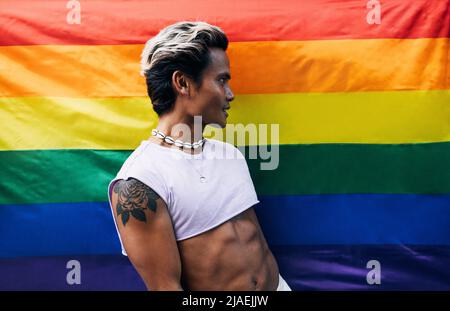 Vue latérale d'un jeune homme élégant se tenant contre le drapeau LGBT et regardant loin Banque D'Images
