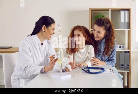 Le médecin amical montre le modèle anatomique de la colonne vertébrale de petite fille debout sur la table dans le bureau du médecin. Banque D'Images