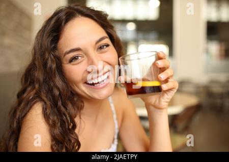 Une femme heureuse dans un bar tenant un verre rafraichissant vous regarde en riant Banque D'Images