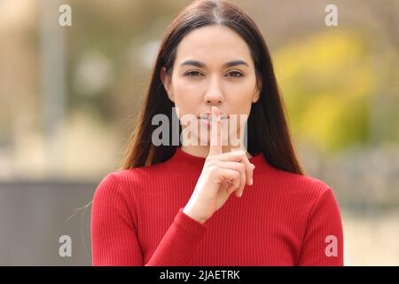 Vue de face portrait d'une femme sérieuse en rouge demandant le silence dans la rue Banque D'Images