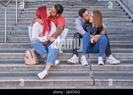 Deux jeunes couples embrassant et embrassant tout en appréciant le temps ensemble assis sur les escaliers à l'extérieur. Concept de relation et d'amour. Banque D'Images
