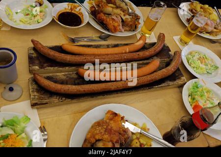 Gros plan sur les saucisses allemandes et les cuisses de porc frite servies avec de la bière glacée, de la salade de coleslaw et des sauces à trempette variées Banque D'Images