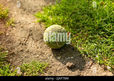 balle de tennis jaune sale sur la route de terre et l'herbe Banque D'Images