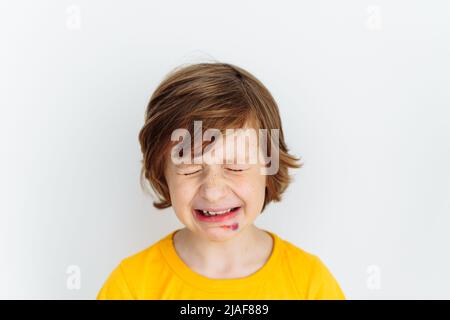 Portrait d'un garçon d'école, un enfant qui pleure en raison d'une plaie mal meurtrisée sur son visage. Un écolier de race blanche en t-shirt jaune pleure de douleur alors qu'il lui fait mal Banque D'Images