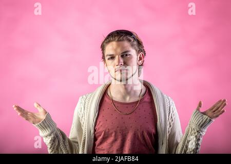 Portrait d'un jeune homme avec barbe et maquillage sur le visage tenant les bras relevés et regardant avec un aspect virilité sur fond rose, prise en studio Banque D'Images