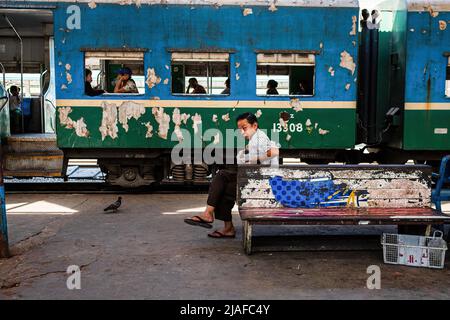 Un homme est assis sur un banc à la gare centrale de Yangon. Train Circle, Yangon Circular Railway, Daily Life dans les rues animées de Yangon. Yangon, l'ancienne capitale du Myanmar, est toujours la plus grande ville et le centre industriel et commercial du pays. La vie quotidienne dans les rues animées et les principaux sites de Yangon, l'ancienne capitale du Myanmar. La ville est toujours la plus grande et le centre industriel et commercial du pays. Banque D'Images