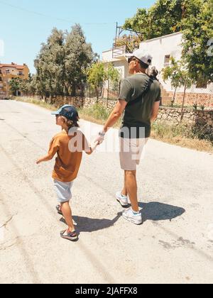 Un père d'homme papa tenant sa main de garçon d'école d'enfant tout en prenant une promenade dehors lors d'une journée chaude ensoleillée Banque D'Images
