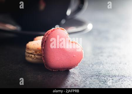 Macarons doux en forme de cœur sur une table noire. Banque D'Images