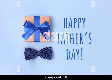 Bonne journée des Pères. Placette festive avec boîte cadeau et noeud papillon. Présenter attaché avec un ruban sur un fond bleu. Banque D'Images