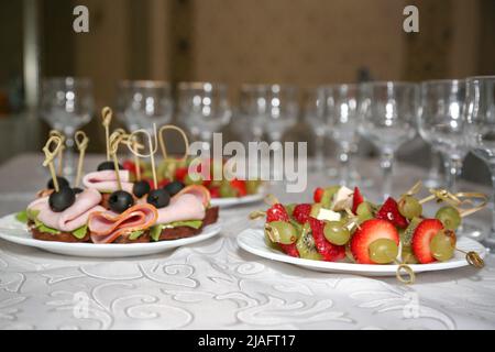 Assiettes avec en-cas sur brochettes et verres vides sur une table recouverte d'une nappe blanche, le concept du début de la fête. Banque D'Images