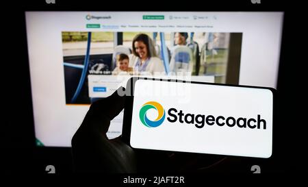 Personne tenant un smartphone avec le logo de la société d'autobus britannique Stagecoach Group plc à l'écran devant le site Web. Mise au point sur l'affichage du téléphone. Banque D'Images