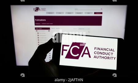 Personne tenant un téléphone portable portant le logo de la British Financial Conduct Authority (FCA) à l'écran devant la page Web. Mise au point sur l'affichage du téléphone. Banque D'Images