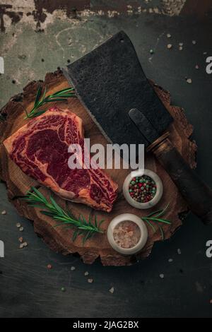 plateau de table de steak sanglant non cuit sur une ancienne planche à découper en bois avec poivre coloré et sel de l'himalaya, romarin et couteau à laver sur le dessus Banque D'Images