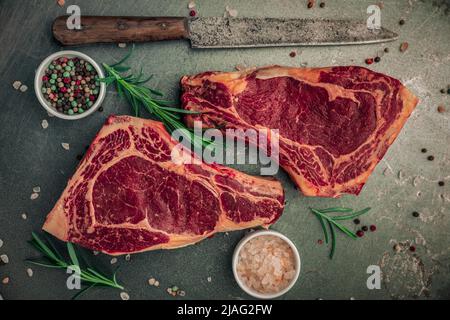 concept alimentaire de délicieux dîner préparé avec deux steaks rouges non cuits avec quelques saupoudrés de sel et de poivre, romarin et bols d'ingrédients Banque D'Images