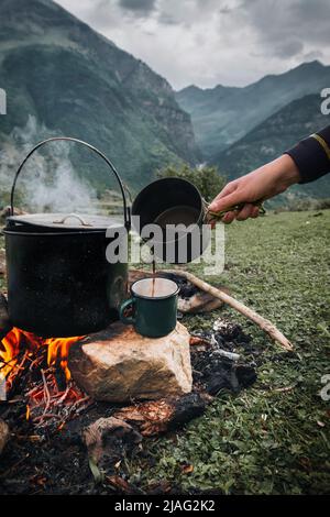 Grande marmite ou chaudron sombre, poêle avec eau bouillante à l'intérieur au-dessus du feu quelque part dans le parc ou les montagnes, concept de camping Banque D'Images