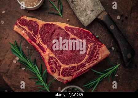 vue de dessus de steak rouge avec herbes et bols de sel rose et poivre coloré sur le dessus de la planche à découper en bois avec un grand couteau à laver, concept alimentaire Banque D'Images