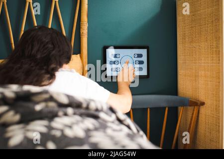 Femme contrôlant la température de la chambre à coucher par le biais d'un appareil de domotique tout en étant couché sur le lit Banque D'Images