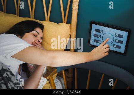 Femme bâillant tout en utilisant un appareil d'automatisation domestique sur le mur dans la chambre Banque D'Images