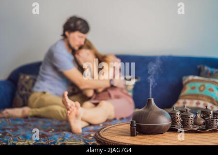 Homme réconfortant son partenaire contrarié à la maison dans le salon. Concept d'aromathérapie. Diffuseur et humidificateur d'huile essentielle à ultrasons en bois électrique Banque D'Images