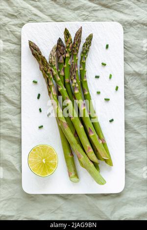 Tiges d'asperges sur l'assiette blanche servies avec du citron vert et de la ciboulette coupée Banque D'Images