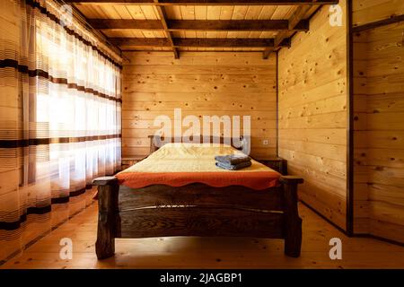 Un lit en bois rustique dans une confortable chambre de style cottage avec un lit double, une table de chevet, des couvertures et des serviettes. Banque D'Images