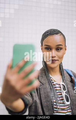 Femme souriante aux cheveux tressés prenant le selfie à travers le smartphone Banque D'Images
