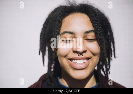 Joyeux jeune genderqueer personne debout avec les yeux fermés pendant la journée ensoleillée Banque D'Images