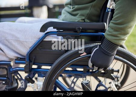 Gros plan d'un adolescent portant des gants de protection en fauteuil roulant dans le parc Banque D'Images