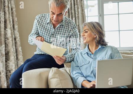 Souriant couple d'âge mûr à la maison examen des finances domestiques sur ordinateur portable Banque D'Images