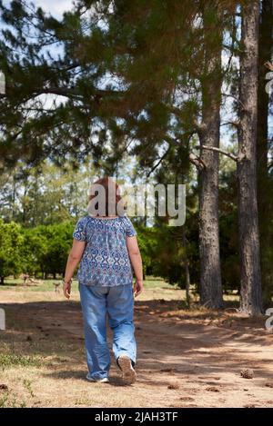 Femme vue de l'arrière marchant seul le long d'une route de campagne pendant un après-midi d'été. Concepts : tourisme rural, vie active, profiter du plein air. Banque D'Images