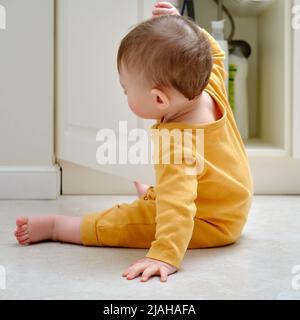 Bébé garçon joue avec des détergents et des produits de nettoyage dans une armoire de cuisine ouverte. Problèmes de sécurité des enfants dans la chambre d'accueil, petit enfant Banque D'Images