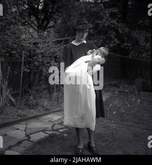 1950s, historique, baptisant, une élégante dame anglaise dans un chapeau, une mère, debout, à l'extérieur, tenant son bébé, Qui est vêtu d'une longue dentelle châle Angleterre, Royaume-Uni. Banque D'Images