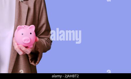 Femme enseignante tenant une banque de porc dans ses mains sur fond bleu, bannière de près Banque D'Images