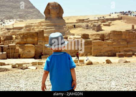 Giza, Egypte, juin 27 2017 : enfant touristique dans le plateau de Giza sur la rive ouest du Nil face à un Sphinx flou et aux pyramides de l'ancien W Banque D'Images