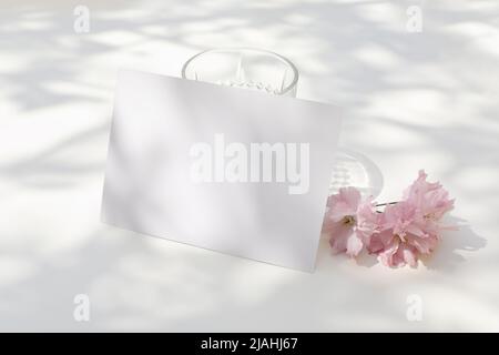 Papeterie de mariage de printemps. Fleur de cerisier japonais rose et verre d'eau en plein soleil. Carte de vœux vierge, invitation. Entreprise Banque D'Images